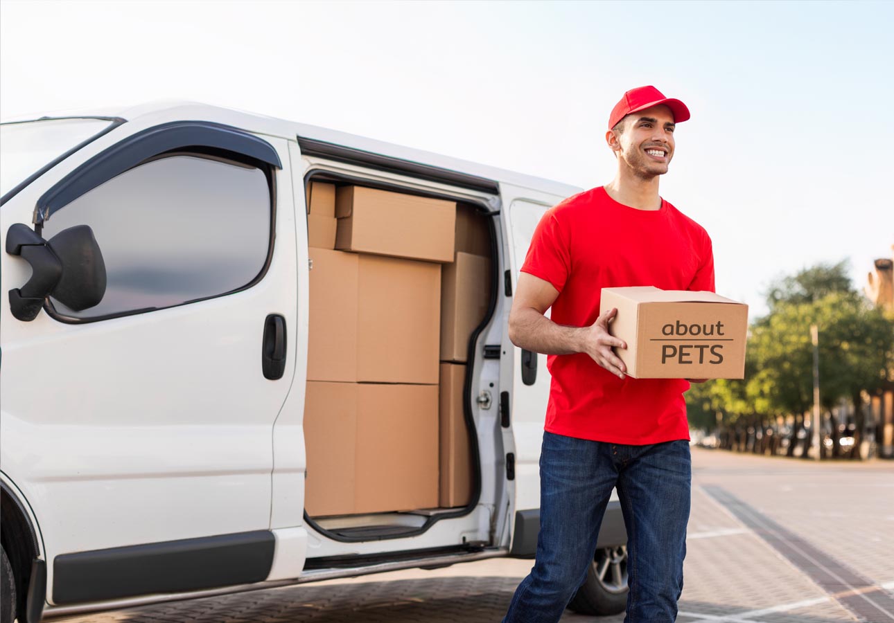 Delivery person in red shirt and cap holding a box labeled 'about PETS' next to a white delivery van with open cargo door