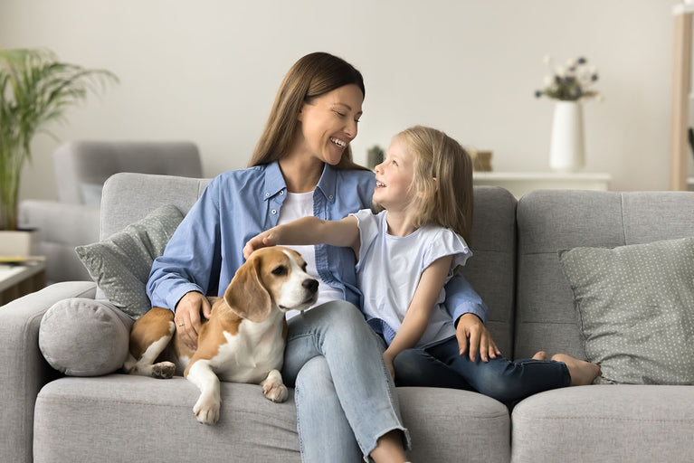 Happy woman and child sitting on a couch with a gorgeous dog in a living room.