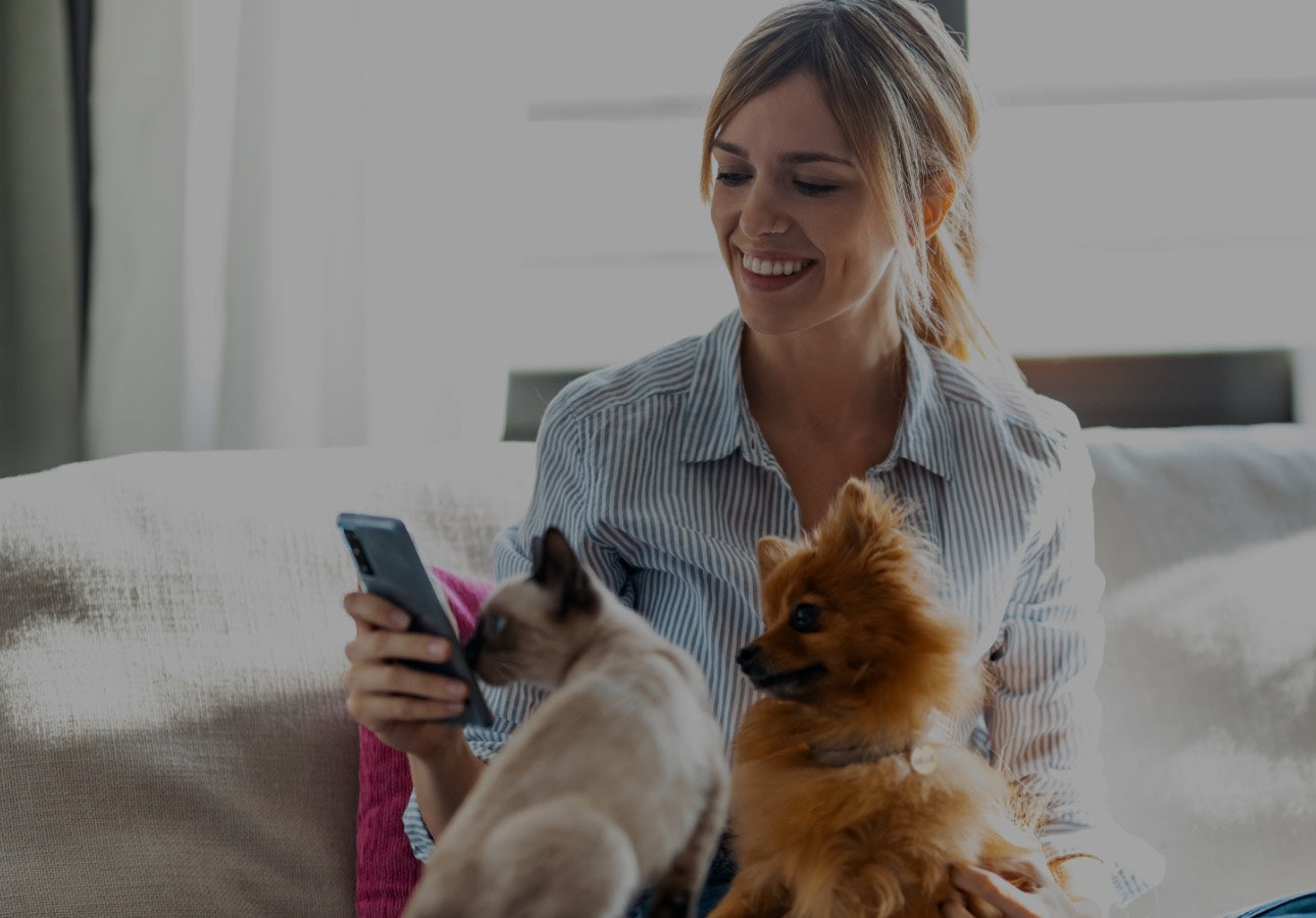 Woman with a cat and dog with About Pets name ID tags using a smart phone.